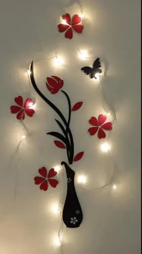 Decorative wall art with red flowers, black vase, and butterfly, illuminated by string lights on a white background.