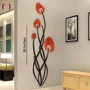 Decorative wall art with red flowers and black branches on a gray wall, with a wooden cabinet and framed pictures in the background.