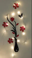 Decorative wall art with red flowers, black vase, and butterfly, illuminated by string lights on a white background.