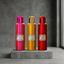 Three Blackberry perfume spray bottles in pink, gold, and red, standing on a gray stone slab against a textured gray background.