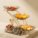 Three-tiered gold fruit basket with fruits on a neutral background