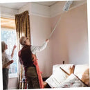 Person cleaning a window with a long-handled tool in a room with a couch and curtains.