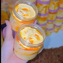 Two jars with a swirled orange and white substance, held by a hand against a colorful background.