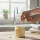 Person applying cream from a jar on a wooden surface with a blurred background